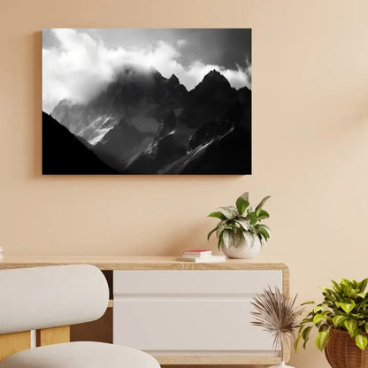 Un "Tableau Montagnes Rocheuses Paysage Alpes Noir et Blanc" est accroché sur un mur beige au-dessus d'un bureau en bois avec tiroir et armoire, décoré d'une plante et de livres.