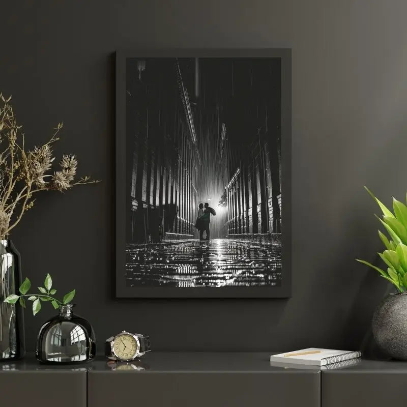 Tableau Photo Noir et Blanc Couple Sous La Pluie, joliment encadré et affiché sur un mur sombre, avec des plantes, un bocal en verre, une montre et un cahier ornant l'étagère en dessous.