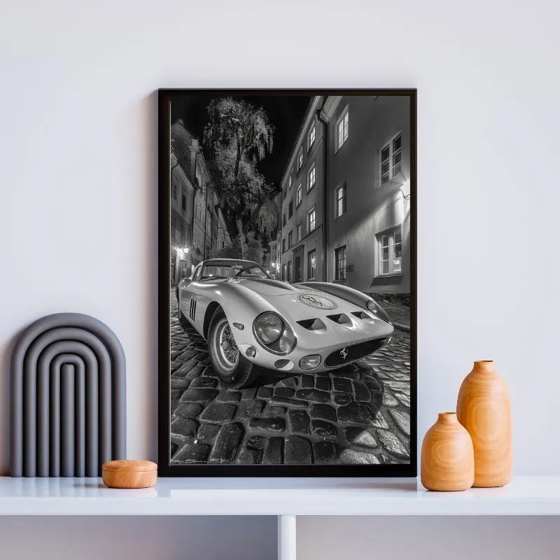 Encadré **Tableau Ford GT Ruelle Pavée Monochrome** d'une Ford GT vintage sur une rue pavée la nuit, exposée sur une étagère moderne avec des vases décoratifs.