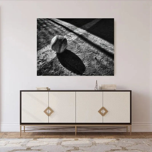 Un Tableau Balle Baseball Terrain Noir et Blanc encadré et suspendu au-dessus d'une console moderne beige et noire, crée une ambiance sophistiquée. La table, avec ses deux poignées en forme de losange, ajoute une touche élégante à cette décoration sportive.