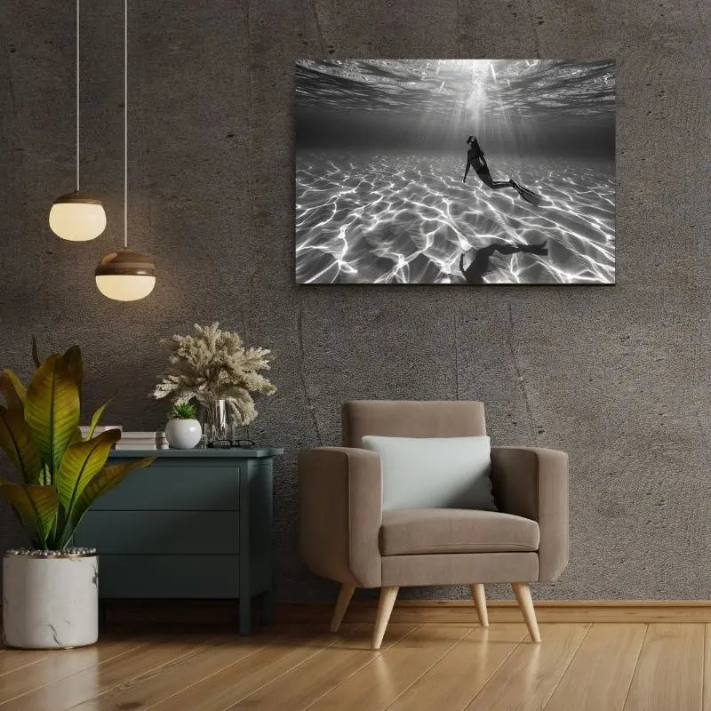 Un salon moderne présente un mur texturé gris, un fauteuil avec un coussin, une petite table d'appoint avec des plantes et le *Tableau Plongeuse Fond Sous Marin Noir et Blanc* ornant le mur.