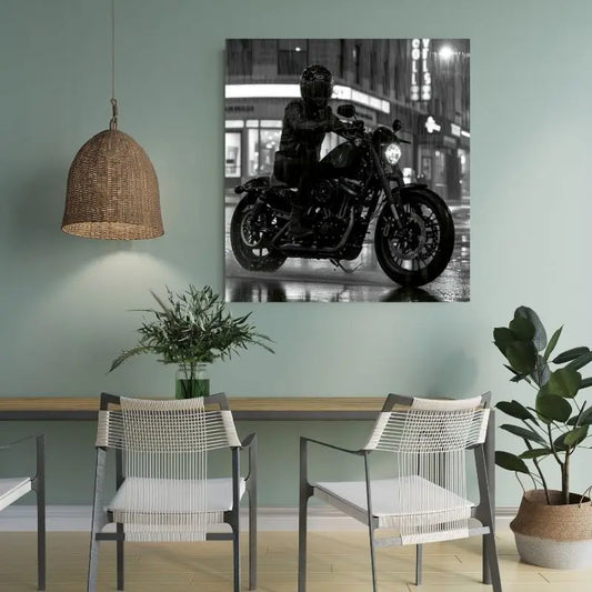 Une photographie accrochée au mur, intitulée Tableau Moto Virée Urbaine Nocturne Monochrome, représente un motocycliste roulant dans un décor urbain pluvieux la nuit, ajoutant une touche de noir et blanc. La pièce comprend deux chaises blanches, une plante et un luminaire suspendu tissé, qui contribuent tous au décor moderne.