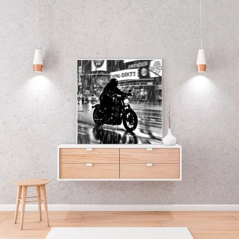 Le Tableau Motard Ville Pluvieuse Nuit Noir et Blanc représentant un motard roulant sous la pluie est exposé sur un mur gris clair au-dessus d'une étagère en bois à deux tiroirs, ajoutant une ambiance urbaine à la décoration intérieure.