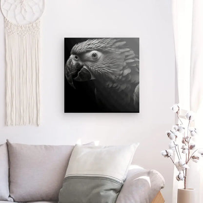 Une photo en noir et blanc, intitulée "Tableau Perroquet Noir et Blanc Ara Portrait Oiseau Parot", est accrochée sur un mur blanc au-dessus d'un canapé gris clair avec des oreillers blancs et crème. À côté se trouvent une tenture murale en macramé et un vase avec des tiges de coton.