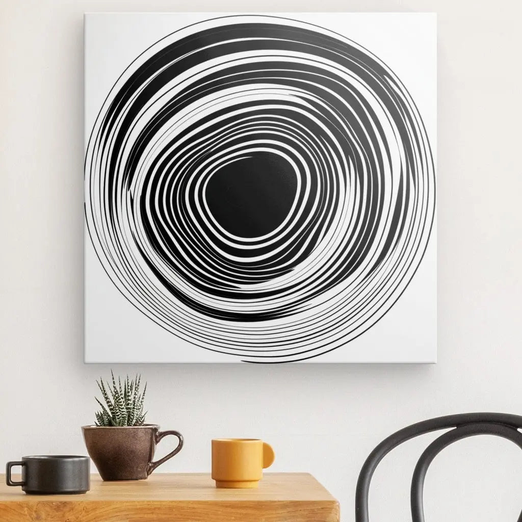 Une peinture monochrome moderne Tableau Noir et Blanc Minimaliste Cercle Vinyle Abstrait suspendue au-dessus d'une table en bois avec une tasse, une petite plante en pot et une partie d'une chaise en métal visible.