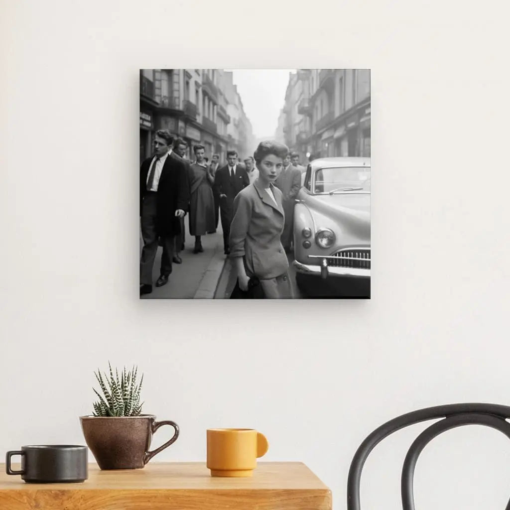 Un Tableau Portrait Femme Photo Vintage New York Noir et Blanc sur un mur représente un portrait féminin vintage d'une femme marchant dans une rue de la ville à proximité de voitures garées. Au premier plan, une table en bois avec une plante et deux mugs. Une chaise est partiellement visible à droite.