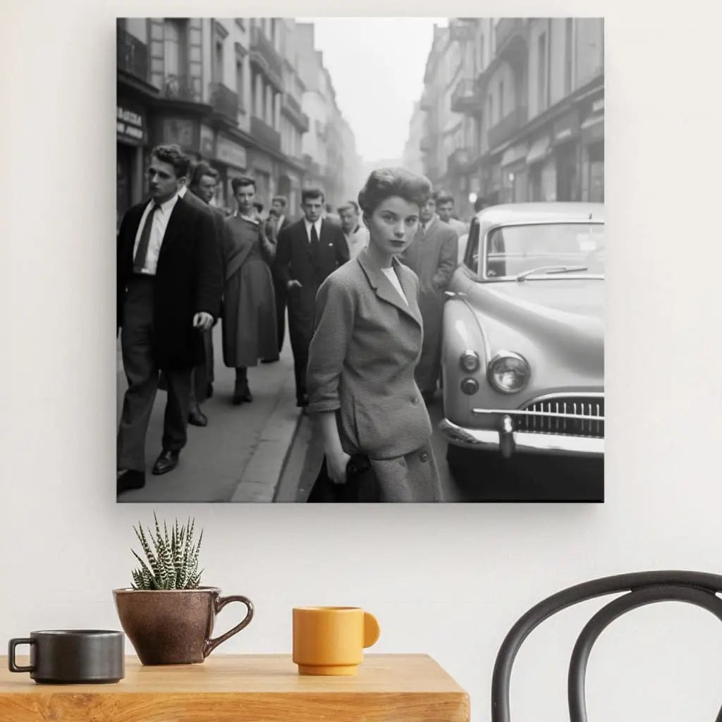 Un superbe Tableau Portrait Femme Photo Vintage New York Noir et Blanc capture une femme à la mode du milieu du XXe siècle, debout dans une rue animée de la ville avec des piétons et une voiture classique en arrière-plan. Cette photographie vintage saisissante est exposée au-dessus d’une petite table avec des tasses.