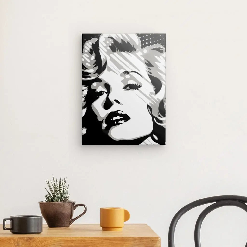 Un Tableau Portrait Marilyn Pop Art Toile Noir et Blanc est accroché sur un mur blanc au-dessus d'une table en bois avec deux tasses, une petite plante et une chaise noire, créant un tableau Pop Art saisissant.