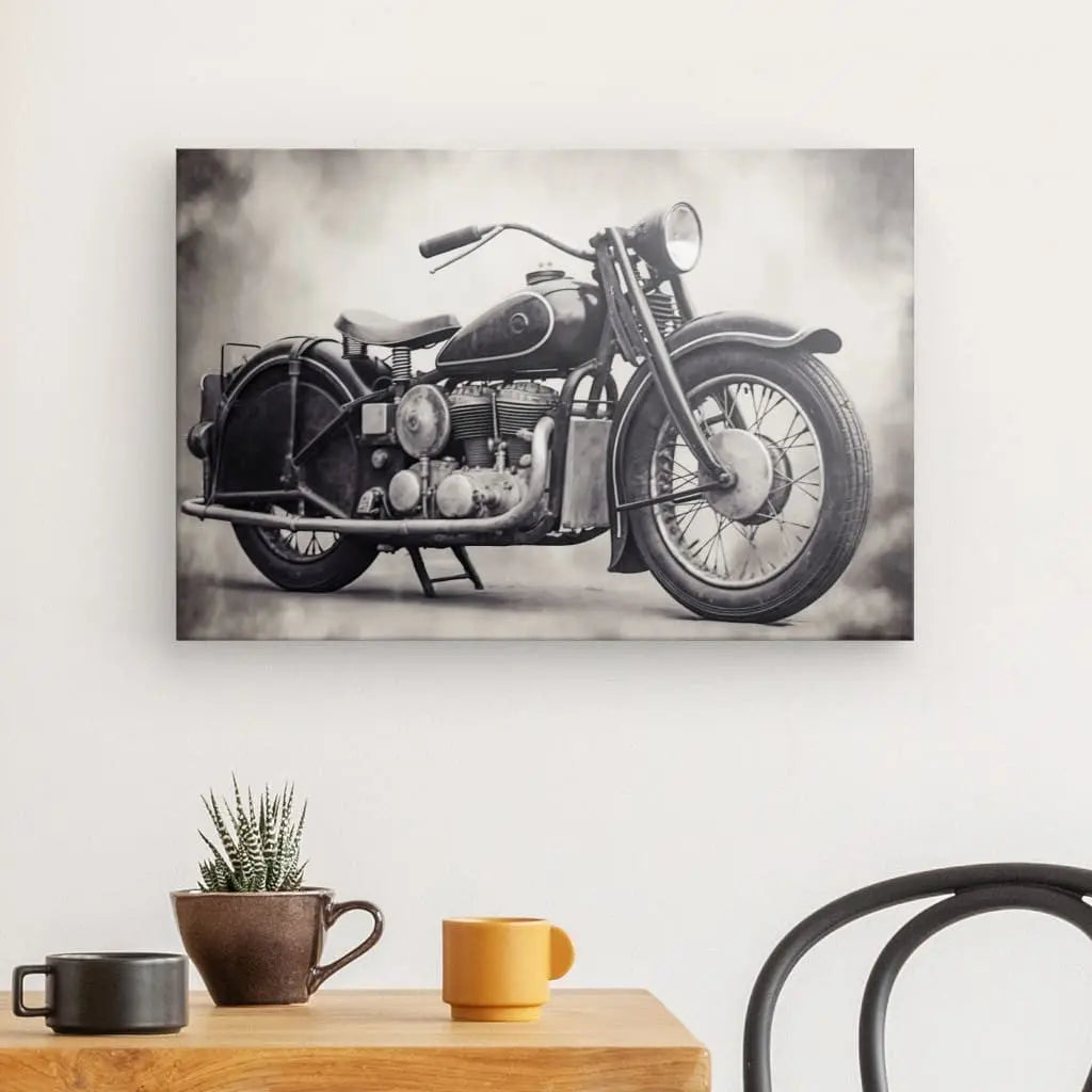 Une photographie en noir et blanc d'un Tableau Moto Vintage Moteur Rétro Style Harley Noir et Blanc est exposée sur un mur au-dessus d'une table en bois avec une petite plante en pot, une tasse marron et une tasse jaune. Une chaise noire est partiellement visible.