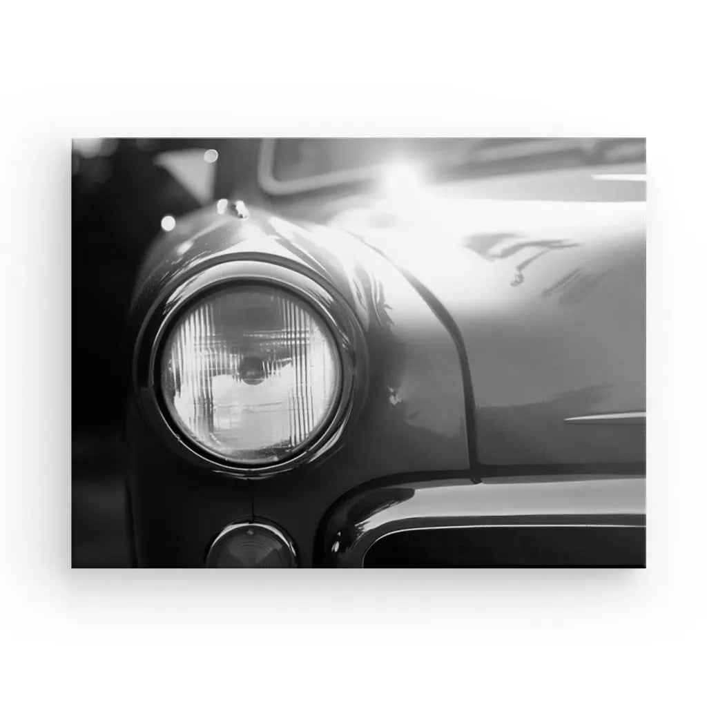 Gros plan noir et blanc du phare avant et de la calandre partielle d'une voiture d'époque, avec la lumière se reflétant sur le capot. Cette image époustouflante capture l'essence du Tableau Voiture Ancienne Phare Rond Vintage Design Noir et Blanc dans une esthétique noir et blanc intemporelle.