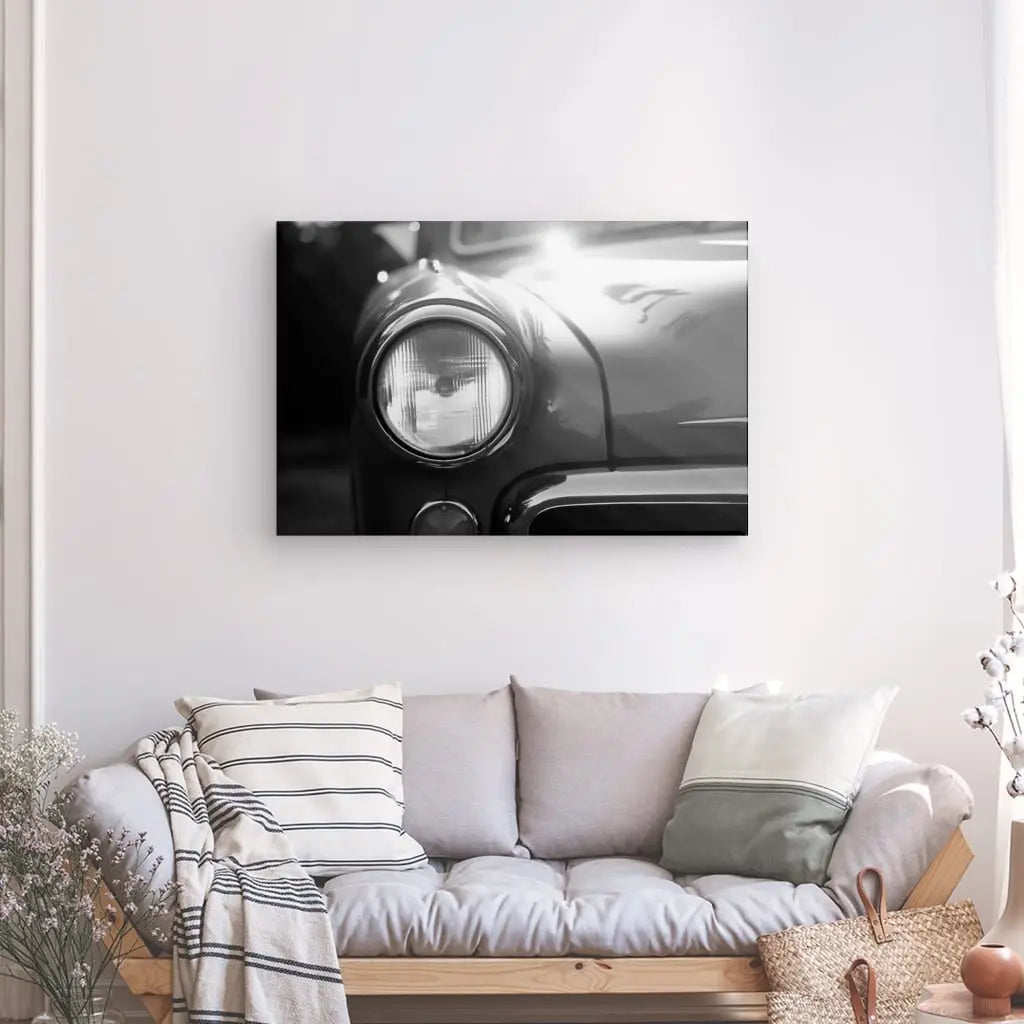 Un salon dispose d'un canapé gris clair avec des oreillers et une couverture. Une photographie en noir et blanc d'un Tableau Voiture Ancienne Phare Rond Vintage Design Noir et Blanc est affichée sur le mur au-dessus du canapé.