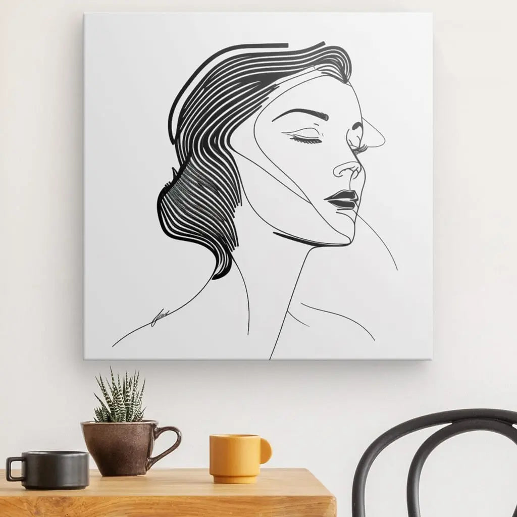 Un Tableau Portrait Femme Diva Dessin Moderne Visage Traits Noir et Blanc est exposé sur un mur blanc au-dessus d'une table en bois avec une petite plante en pot et deux tasses, et une chaise noire est partiellement visible à droite.