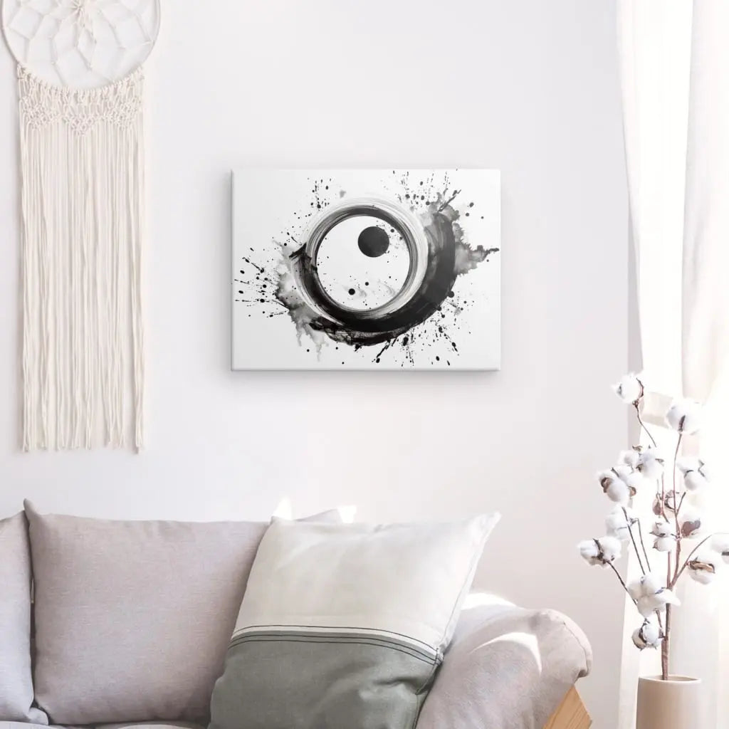 Un mur blanc du salon présente un Tableau Moderne Noir et Blanc Cercles Eclaboussures Peinture Monochrome avec une peinture abstraite, une branche de coton dans un vase, un canapé gris avec des oreillers blancs et gris et une tenture murale en macramé.