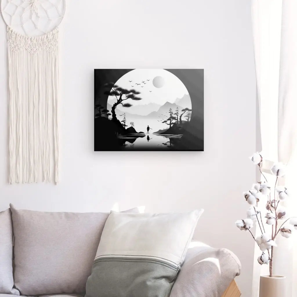 Un art mural Tableau Paysage Onirique Dessin Noir et Blanc Asie représentant un paysage onirique serein avec une grande lune, des arbres et un petit bateau sur une rivière. Il est suspendu au-dessus d'un canapé de couleur claire avec des coussins, à proximité d'une tenture murale en macramé et d'un vase.