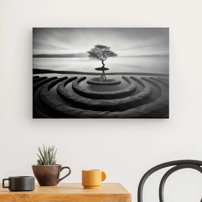 Un Tableau Paysage Zen Arbre Calme Photo Noir et Blanc d'un Arbre Calme solitaire sur une île dans des ondulations de sable concentriques est accroché à un mur au-dessus d'une table en bois avec une plante en pot, une tasse jaune, une tasse orange et une chaise noire.