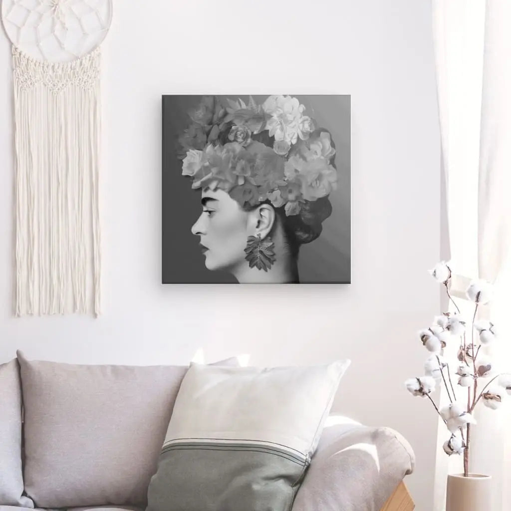 Un salon avec un canapé gris, un coussin blanc, une tenture murale et un Tableau Profil Frida Fleurs Cheveux Rose Pivoine Portrait Noir et Blanc d'une personne avec des fleurs sur la tête. Une branche avec des capsules de coton se dresse à droite, créant un tableau art contemporain qui respire la simplicité chic.