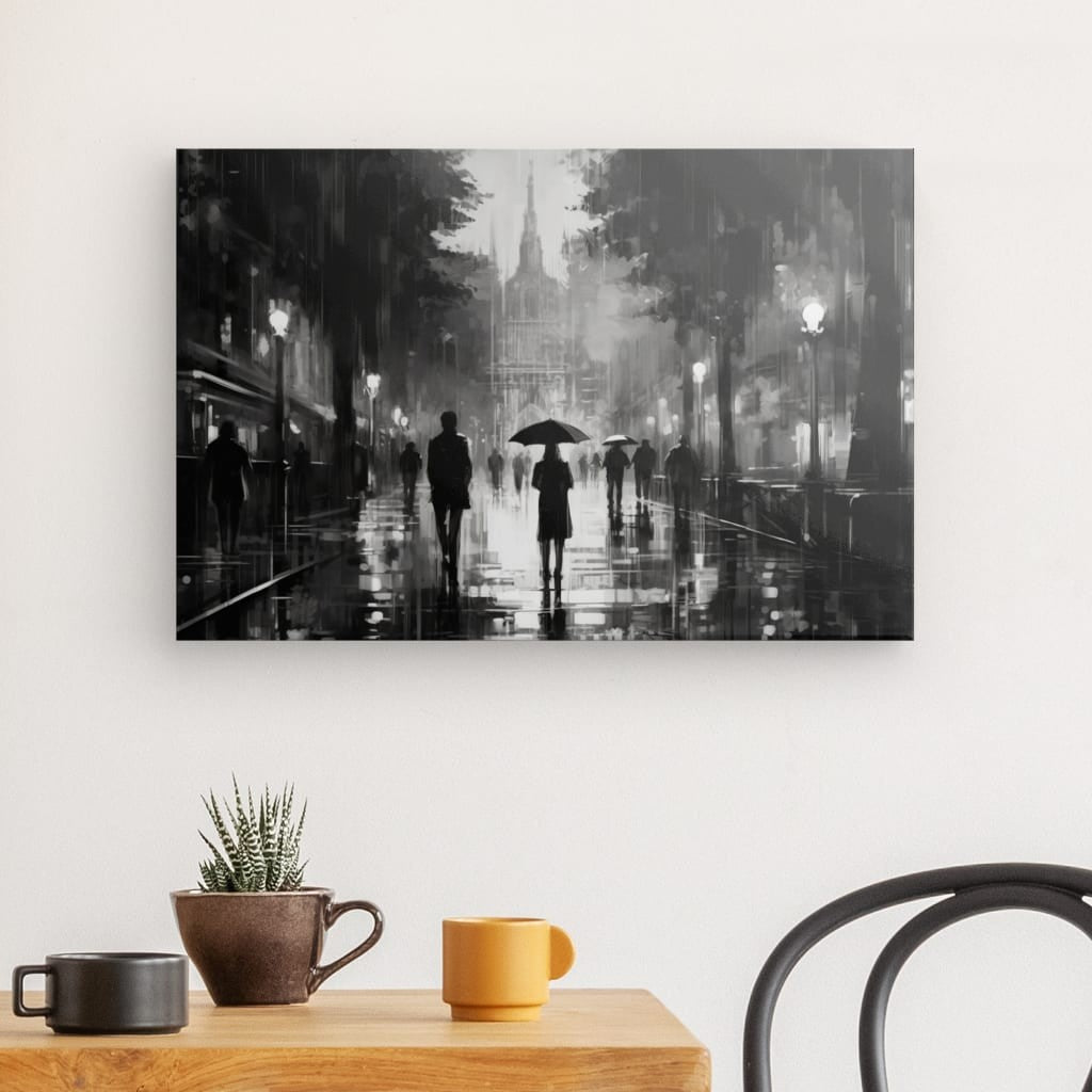 Un Tableau Peinture Femme Sous la Pluie Noir et Blanc encadré représente des personnes marchant avec des parapluies dans une rue pluvieuse de la ville, accrochées à un mur blanc au-dessus d'une table avec un petit cactus et deux tasses.