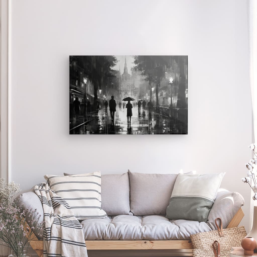 Un Tableau Peinture Femme Sous la Pluie Noir et Blanc mural représentant une scène de rue pluvieuse représentant une peinture femme sous la pluie est suspendu au-dessus d'un canapé gris avec des coussins rayés et unis, dans un salon orné d'un panier et de plantes.