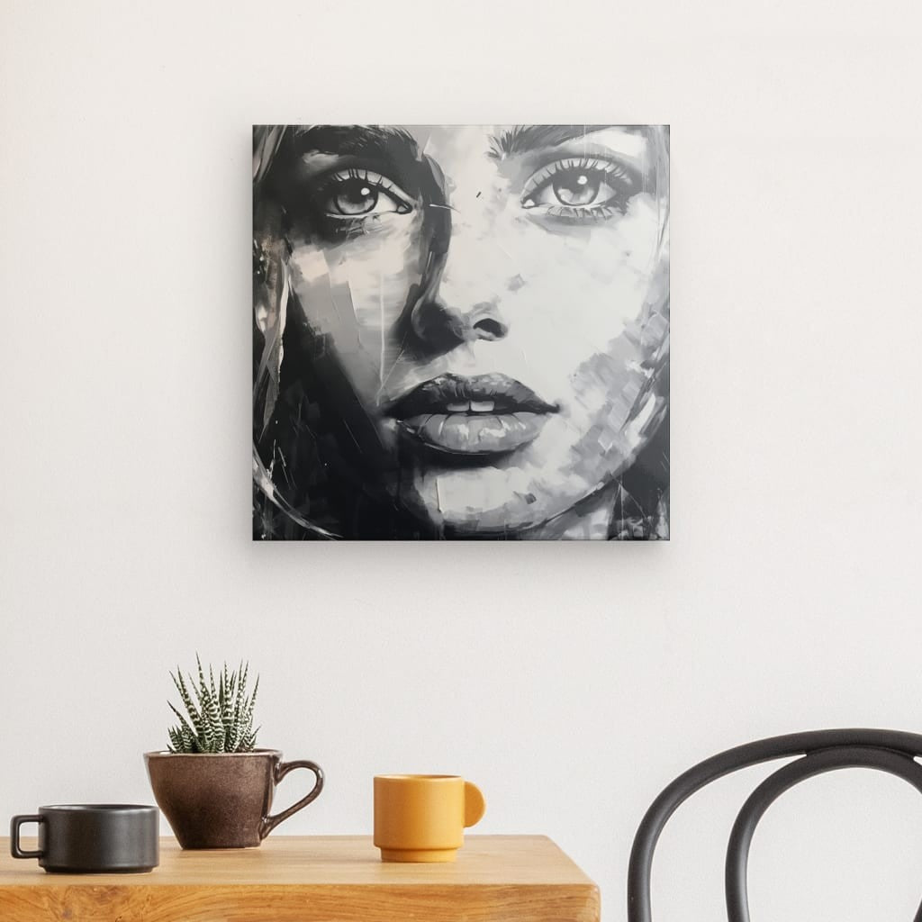 Un Tableau Peinture Visage Portrait Femme Moderne Noir et Blanc est accroché sur un mur blanc au-dessus d'une table en bois avec une tasse marron, une tasse jaune et une petite plante en pot. Une chaise noire est partiellement visible.