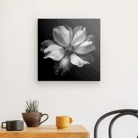 Un Tableau Photo Fleur Blanche Rosée Macro Minimaliste Noir et Blanc est accroché sur un mur blanc au-dessus d'une table en bois. Sur la table se trouvent une tasse marron, une tasse jaune et une petite plante en pot, complétant toutes la nature sereine de la scène, tandis qu'une chaise est assise sur le côté.