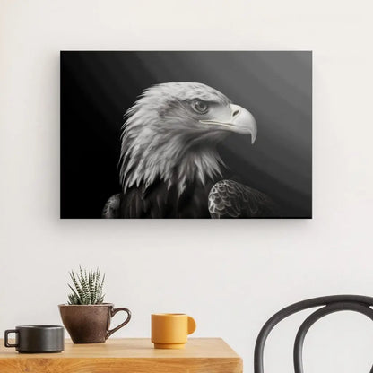 Un Tableau noir et blanc Aigle Royal Portrait Oiseau Noir et Blanc est accroché sur un mur blanc au-dessus d'une table en bois avec deux tasses, un pot de fleurs marron et une petite plante verte. Une chaise noire est partiellement visible.