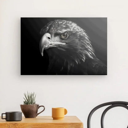 Photographie en noir et blanc d'une tête d'aigle accrochée sur un mur, au-dessus d'une table en bois avec une plante en pot et deux tasses. Ce saisissant Tableau Aigle Rapace Volant Noir et Blanc ajoute une touche de sophistication à l'espace.