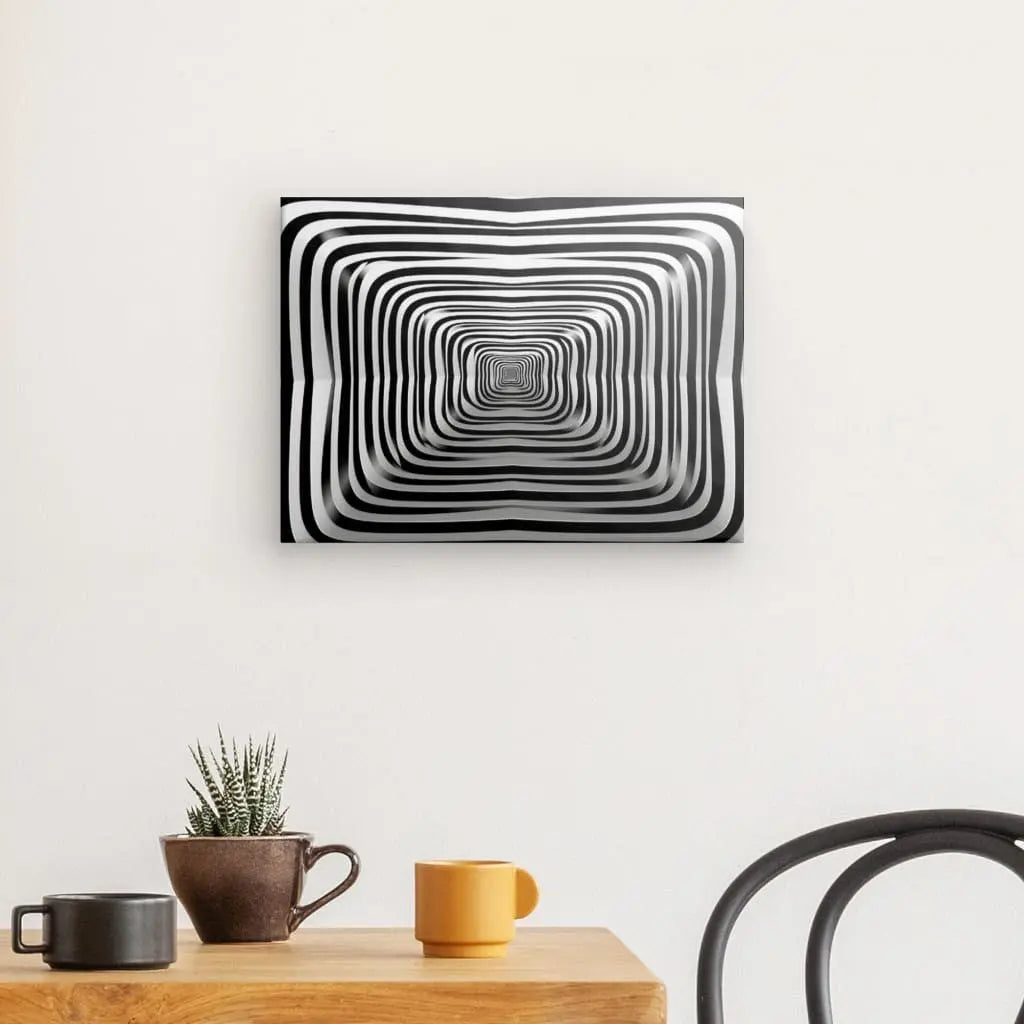 Un tableau Hypnotique Spirale Noir et Blanc Art Abstrait Minimaliste, un véritable art abstrait minimaliste, est suspendu sur un mur blanc au-dessus d'une table en bois avec une petite plante et trois mugs. Une chaise noire est partiellement visible à droite.