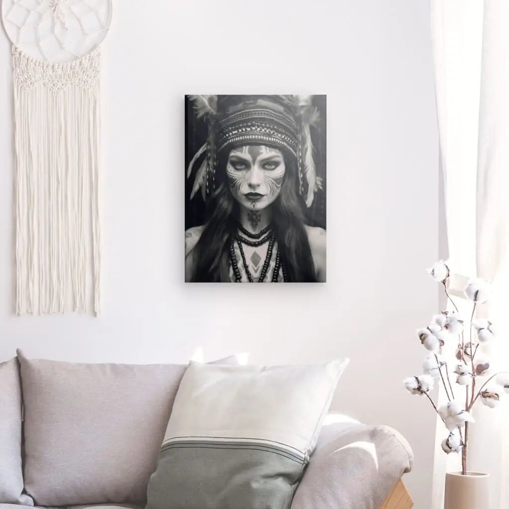 Un Tableau Femme Indienne Portrait Noir et Blanc représentant une personne portant une coiffe et du maquillage est accroché sur un mur blanc au-dessus d'un canapé gris. Une suspension en macramé blanc et une plante font également partie de la décoration de la pièce.