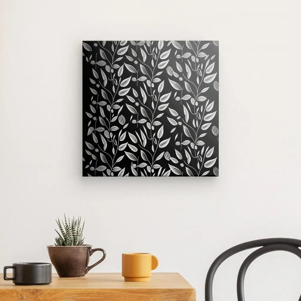 Un Tableau Végétation Plantes Grimpantes Minimalistes Noir et Blanc avec un motif de feuilles blanches est accroché sur un mur blanc au-dessus d'une table en bois avec une plante en pot et deux tasses.