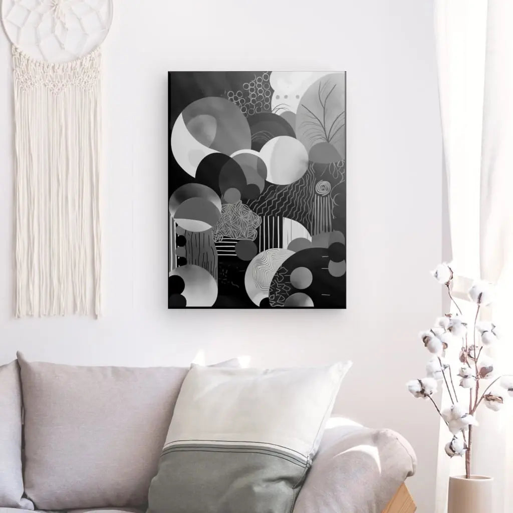 Un salon minimaliste comprend un canapé gris avec des oreillers blancs et gris, une peinture abstraite en noir et blanc sur le mur et une plante en pot avec des fleurs blanches. La décoration moderne est rehaussée par le Tableau Monochrome Cercle Décoration Moderne, ajoutant à l'esthétique globale épurée.