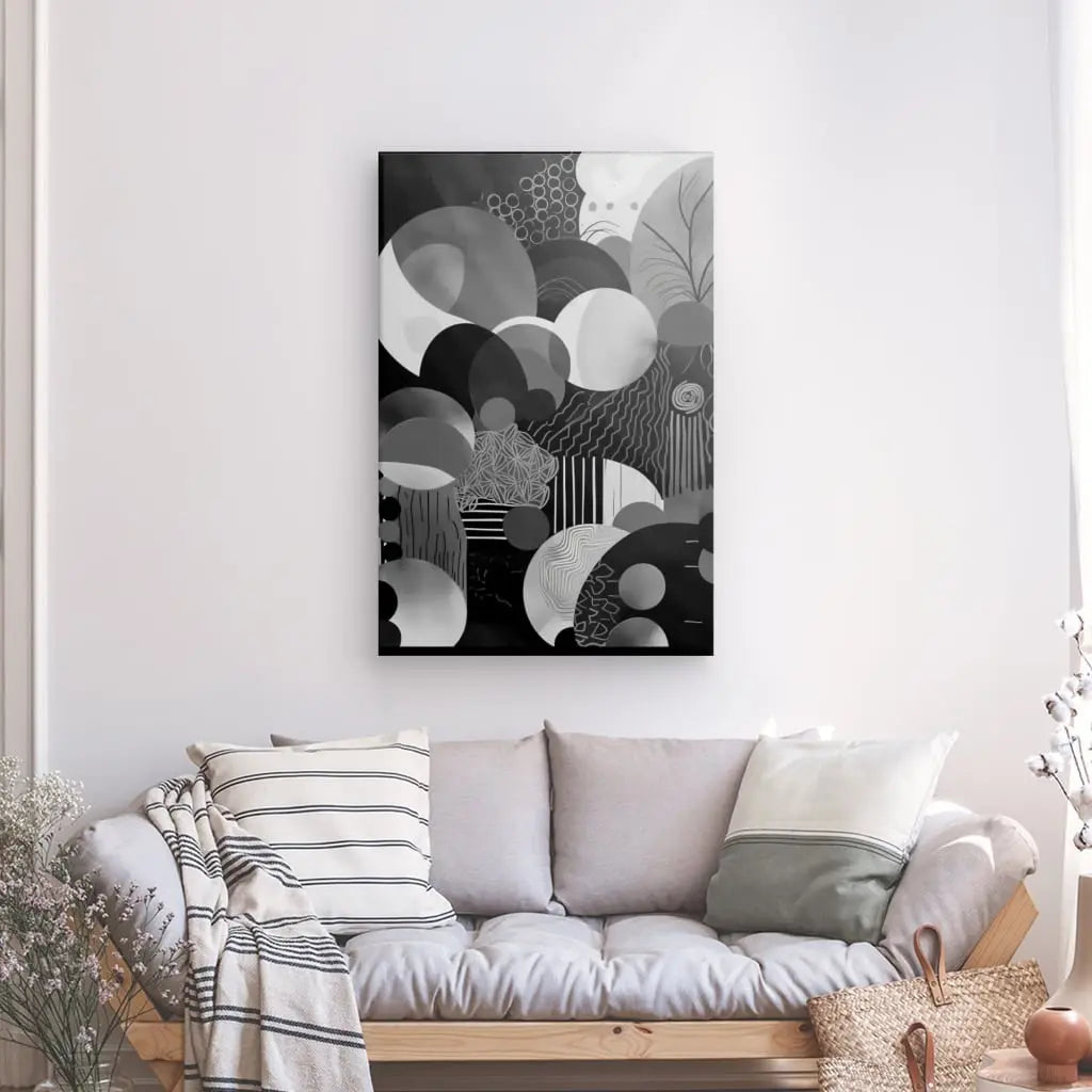 Un Tableau Monochrome Cercle Décoration Moderne aux motifs circulaires et géométriques est suspendu au-dessus d'un canapé gris clair orné de coussins assortis. Un mur blanc forme le décor, et une plante est visible à gauche, ajoutant une touche de décoration moderne à l'espace.