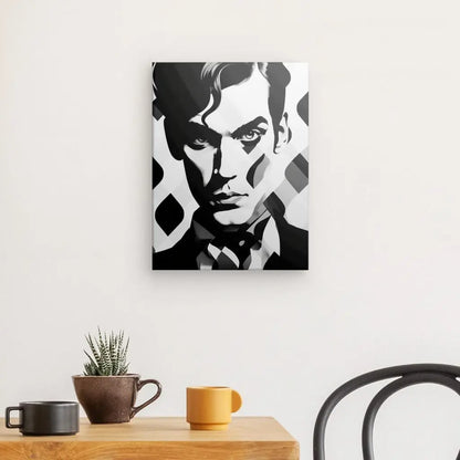 Un portrait en noir et blanc d'un homme à l'air sérieux, ressemblant à un Tableau Homme Moderne Pop Art Monochrome, est accroché sur un mur blanc au-dessus d'une table en bois avec une plante, une tasse et un bol. Une chaise noire est partiellement visible.