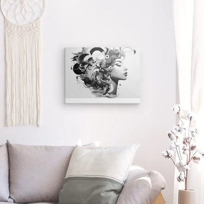 Un Tableau Portrait Patchwork Mélange Noir et Blanc représentant un profil de femme avec des éléments abstraits est accroché sur un mur blanc au-dessus d'un canapé gris clair orné d'oreillers. Une décoration en macramé et un vase avec des tiges de coton sont également visibles.