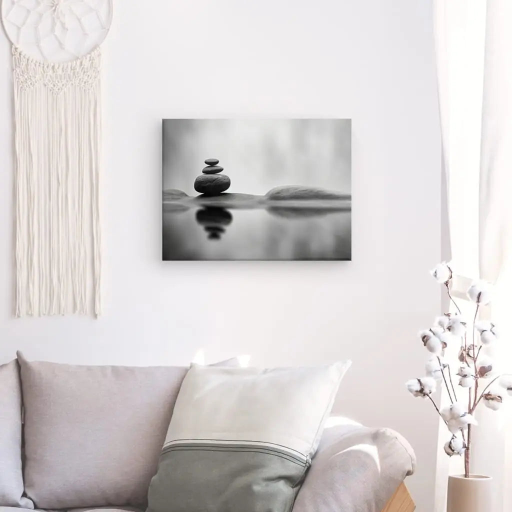 Salon minimaliste avec un canapé gris, des oreillers blancs et gris et un Tableau Relaxant Pierres Ruisseau Paysage Monochrome. Une tenture murale en macramé et une décoration en cotonnier renforcent l'atmosphère de détente et de paix.