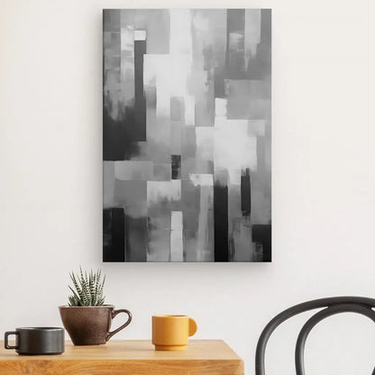 Un Tableau Peinture Abstrait Bandes Effet Flou Noir et Blanc est accroché sur un mur blanc. En dessous se trouve une table en bois avec un petit cactus en pot et deux tasses à café, une noire et une jaune, à côté d'une chaise noire.