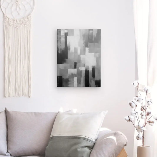 Un salon moderne comprend un canapé gris avec un oreiller blanc et gris, une tapisserie suspendue et un Tableau Peinture Abstraite Bandes Effet Flou Noir et Blanc au-dessus. La lumière naturelle filtre à travers un rideau blanc, créant un effet flou qui adoucit l'espace.
