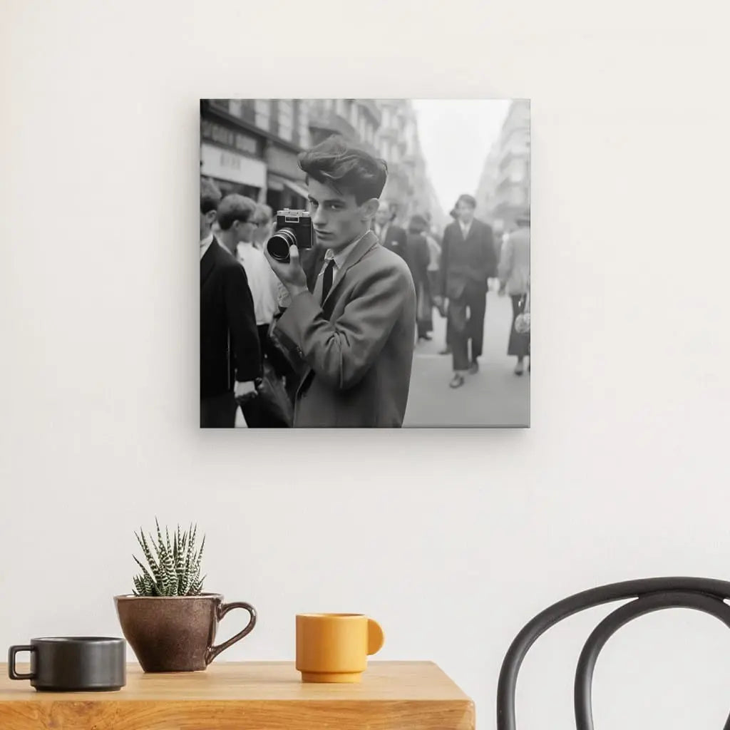 Un Tableau Photographique Vintage Portrait Photographe Urbain représentant une personne tenant un appareil photo est affiché sur un mur blanc au-dessus d'une table en bois avec un petit cactus et deux tasses, créant une ambiance artistique et ludique.