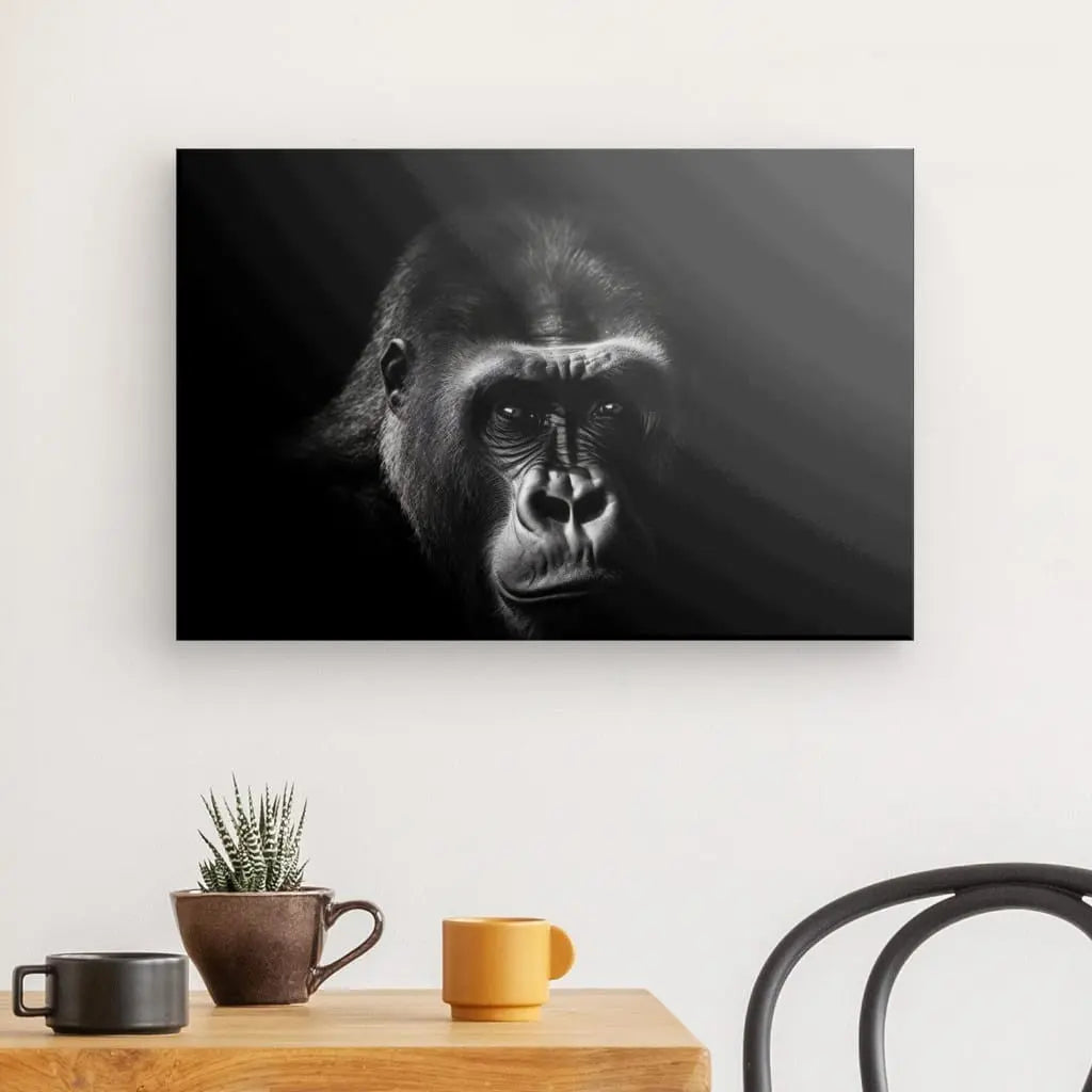 Un Tableau Portrait Gorille Grand Singe Noir et Blanc en noir et blanc est affiché sur un mur blanc au-dessus d'une table en bois avec une plante, une tasse marron, une tasse jaune et une chaise noire. Ce décor ajoute une touche élégante à l'intérieur.