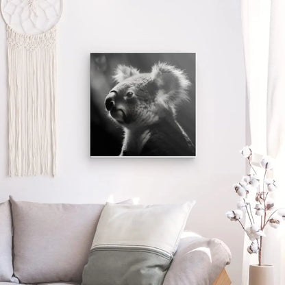 Un Tableau Koala Nature Noir et Blanc encadré est accroché sur un mur blanc au-dessus d'un canapé gris clair avec un oreiller. Un attrape-rêves et une petite plante ajoutent à l'atmosphère de sérénité.