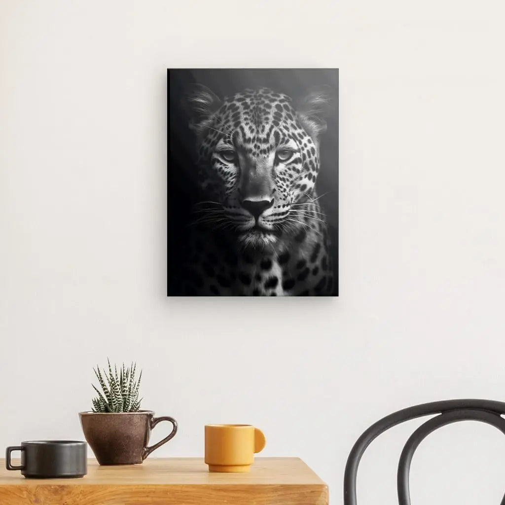 Une photographie en noir et blanc Tableau Panthère Portrait Sauvage Noir et Blanc d'un léopard est accrochée sur un mur blanc au-dessus d'une table en bois avec deux tasses, une petite plante dans un pot et une chaise noire à proximité.