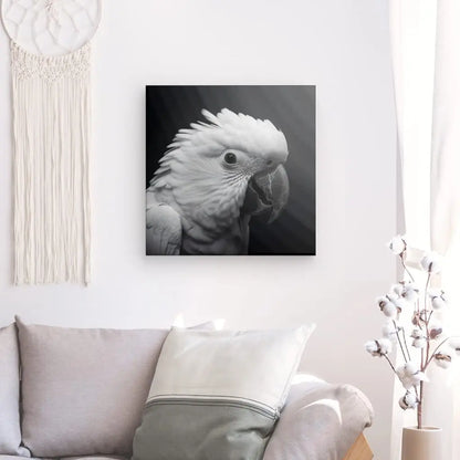 Une photographie d'art noir et blanc détaillée d'un perroquet, étiquetée « Tableau Perroquet Perruche Gros Plan Noir et Blanc », est accrochée sur un mur blanc au-dessus d'un canapé de couleur claire avec un coussin. Une tenture murale en macramé et une plante font également partie du décor.