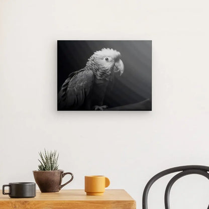 Une saisissante photo en noir et blanc intitulée Tableau Perroquet Oiseau Sauvage Portrait Noir et Blanc est accrochée sur un mur blanc au-dessus d'une table en bois avec une petite plante en pot et deux tasses ; une chaise en bois est partiellement visible.