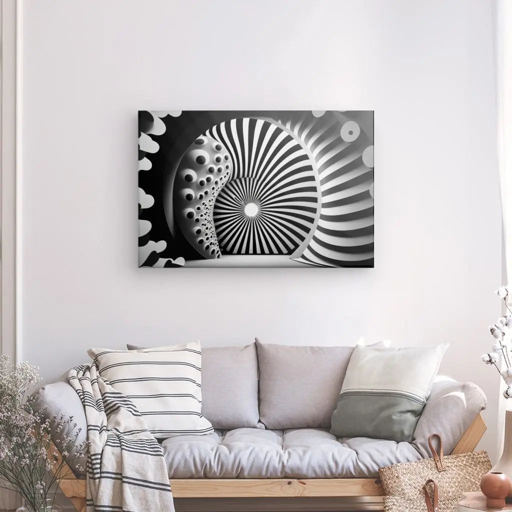 Un canapé beige avec des oreillers rayés et unis se trouve devant un mur orné d'un Tableau Moderne 3D Hypnotique Noir et Blanc. Un vase avec des fleurs se trouve sur le côté gauche et un panier se trouve à droite, complétant la décoration intérieure chic.