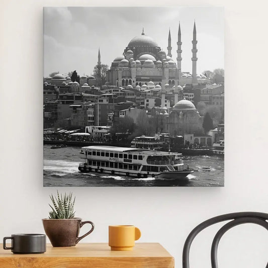 Impression sur toile du Tableau Istambul Paysage Mosquée Turquie Noir et Blanc représentant un ferry sur une rivière avec une grande mosquée en forme de dôme en arrière-plan, imprimée avec des encres latex HP, accrochée au-dessus d'une table avec une tasse et un.