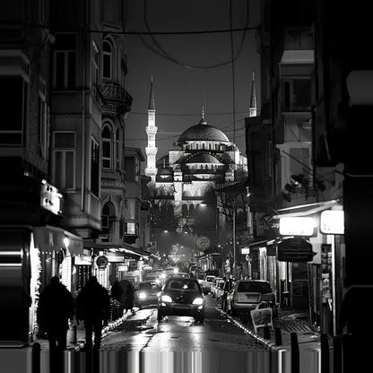 Scène urbaine monochrome de nuit montrant une rue animée menant à une mosquée lointaine illuminée avec des minarets, sous un ciel sombre, capturée dans Tableau Photographie Nocturne Istambul Noir et Blanc.