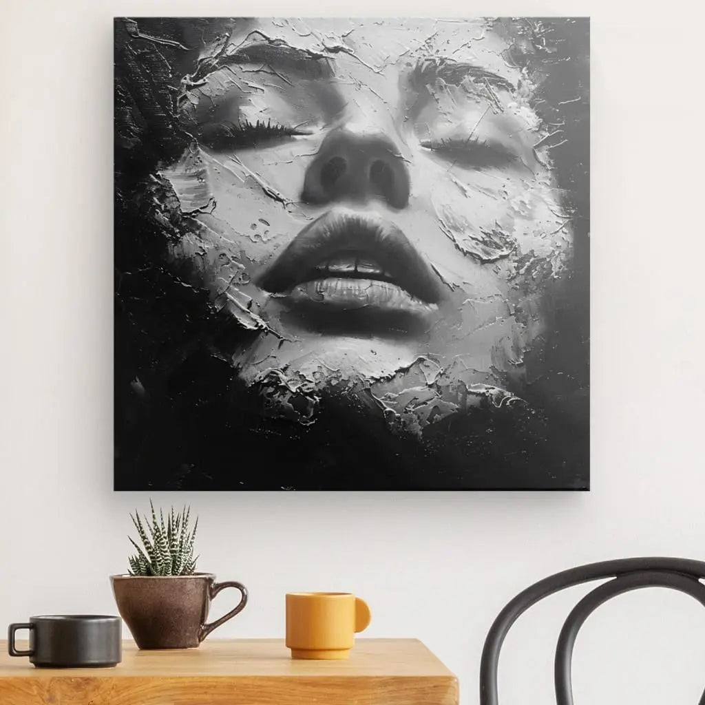 Un Tableau Visage Craquelé Peinture Noir et Blanc représentant un visage de femme fragmenté comme derrière une vitre brisée, enfermé dans un cadre en bois d'épicéa, accroché sur un mur blanc au-dessus d'une table avec une plante et un jaune.