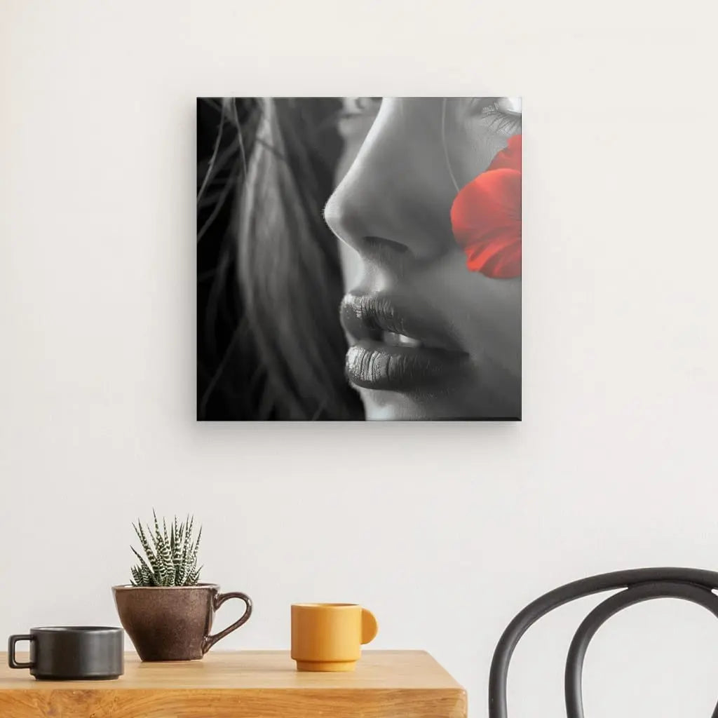 Tableau Portrait Femme Noir et Blanc Fleur Rouge représentant un visage de femme avec une rose rouge près de ses lèvres, imprimé sur une toile blanc brillant à texture fine, accroché à un mur au-dessus d'une table avec une plante et une tasse