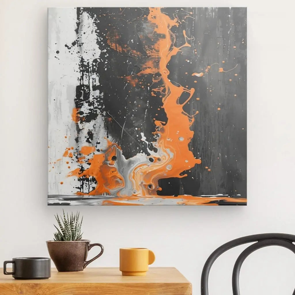 Un Tableau Abstrait Noir et Blanc Touche d'Orange encadré est accroché sur un mur blanc au-dessus d'une table en bois avec deux tasses et une petite plante. Une chaise noire est partiellement visible.