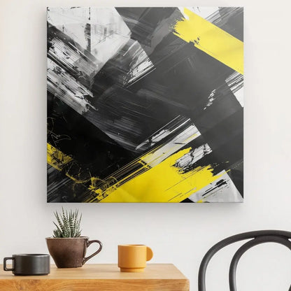 Peinture abstraite avec des coups de pinceau noirs, blancs et jaunes, posée sur un mur blanc au-dessus d'une table en bois avec deux tasses, une petite plante en pot et une chaise partiellement visible. Ce Tableau Noir Blanc Jaune Art Peinture Abstraite ajoute une touche d'art contemporain au cadre serein.