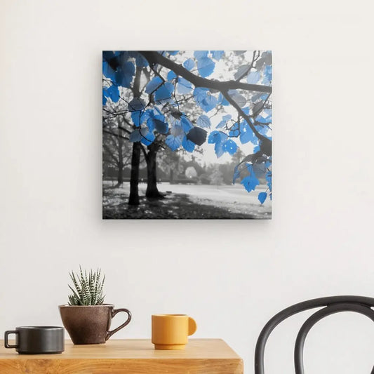 Une pièce avec une table en bois comportant une plante en pot et deux tasses ; le mur affiche une image encadrée du Tableau Nature Noir et Blanc Feuilles Bleues. Une chaise partiellement noire est visible à droite.